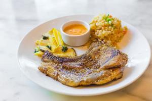 makroaufnahme von schweinenackensteak mit knoblauch gebratenem reis und pfeffersoße einschließlich babymais und pilzen als beilage auf weißem restaurantteller isoliert. foto