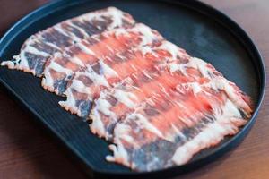 frisches Rindfleisch wurde roh in Scheiben geschnitten für das Restaurant Sukiyaki und Shabu oder Yakiniku serviert, das auf einen schwarzen Teller gestellt wurde. foto