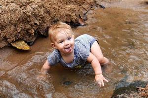 Kleines fröhliches Mädchen mit blonden Haaren im Sommerkleid spielt im Bergfluss. foto