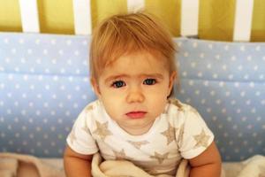 süßes einjähriges Mädchen mit blauen Augen und blonden Haaren wachte gerade in ihrem Bett auf. foto