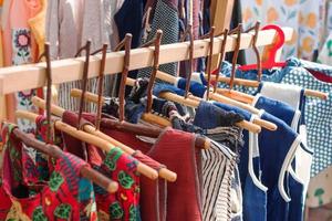 Kleiderständer mit bunten Ethnokleidern aus Baumwolle auf Holzbügeln. Vitrine mit Kleidung auf dem lokalen Straßenmarkt. foto