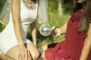 Mädchen im Sommer in Kleidern sitzen auf dem Rasen. Mädchen hält Ball in der Hand. Spiegelkugel in der Handfläche. foto