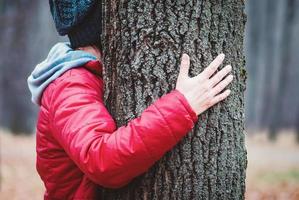 umarmt baumstamm im herbstpark, frau umarmt alten baum im freien, liebe und einheit mit der natur foto