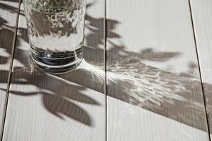 glas wasser auf weißem tisch, schatten und sonnenlicht, kopierraum foto