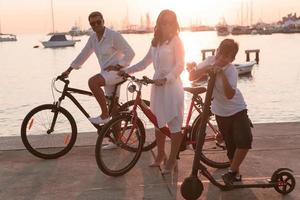 glückliche familie, die zusammen einen schönen morgen am meer genießt, eltern, die fahrrad fahren, und ihr sohn, der einen elektroroller fährt. selektiver Fokus foto