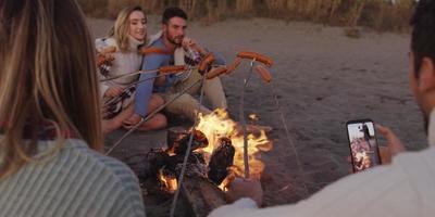 Gruppe junger Freunde, die am Feuer am Strand sitzen foto