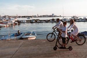 glückliche familie, die zusammen einen schönen morgen am meer genießt, eltern, die fahrrad fahren, und ihr sohn, der einen elektroroller fährt. selektiver Fokus foto