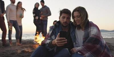 Paar genießt Lagerfeuer mit Freunden am Strand foto