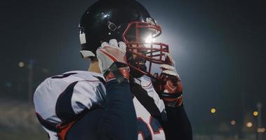 American-Football-Spieler, der einen Helm auf einem großen Stadion mit Lichtern im Hintergrund aufsetzt foto