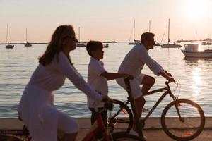 glückliche familie, die zusammen einen schönen morgen am meer genießt, eltern, die fahrrad fahren, und ihr sohn, der einen elektroroller fährt. selektiver Fokus foto