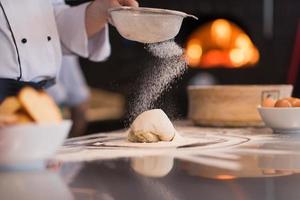 Küchenchef streut Mehl über frischen Pizzateig foto