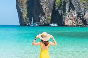 Touristin im gelben Badeanzug und Hut, glücklicher Reisender beim Sonnenbaden am Maya Bay Beach auf der Insel Phi Phi, Krabi, Thailand. wahrzeichen, reiseziel südostasien, urlaub und urlaubskonzept foto