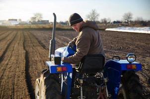 Senior-Bauer, der das Feld auf einem Traktor kultiviert. Saisonarbeiter. Anwerbung von Arbeitskräften für Arbeiten an landwirtschaftlichen Maschinen. Landbewirtschaftung. Landwirtschaft. kleine Bauernhöfe. ländliche Szene. landwirtschaftlicher Betrieb foto