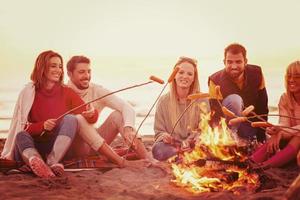 Gruppe junger Freunde, die am Feuer am Strand sitzen foto