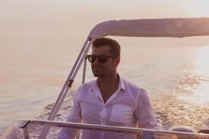 Ein entschlossener Senior-Geschäftsmann in Freizeitkleidung und Sonnenbrille genießt seinen Urlaub mit einem Luxusboot bei Sonnenuntergang. selektiver Fokus foto