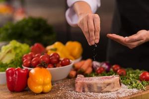 koch, der salz auf eine saftige scheibe rohes steak legt foto