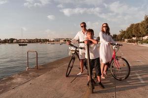 glückliche familie, die zusammen einen schönen morgen am meer genießt, eltern, die fahrrad fahren, und ihr sohn, der einen elektroroller fährt. selektiver Fokus foto