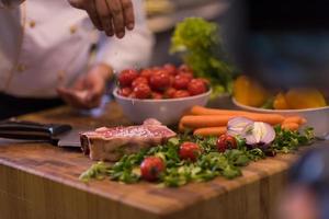 koch, der salz auf eine saftige scheibe rohes steak legt foto