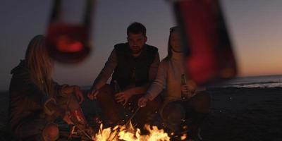 junge freunde, die am lagerfeuer am strand mit bier anstoßen foto