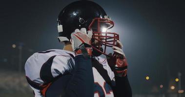 American-Football-Spieler, der einen Helm auf einem großen Stadion mit Lichtern im Hintergrund aufsetzt foto