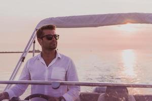 Ein entschlossener Senior-Geschäftsmann in Freizeitkleidung und Sonnenbrille genießt seinen Urlaub mit einem Luxusboot bei Sonnenuntergang. selektiver Fokus foto