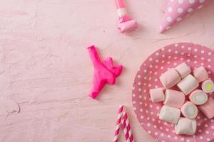 geburtstagsfeierhintergrund, konfettirand, süßigkeiten, lutscher und geschenk auf rosa oberfläche, kopierraum, draufsicht foto