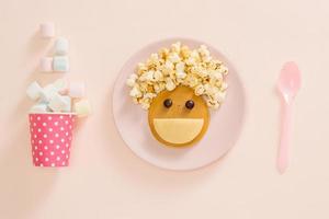 Baby-Pfannkuchen zum Frühstück. kreative idee für das kinderdessert leckere pfannkuchen in form des fröhlichen gesichts mit den haaren, die popcorn machen foto