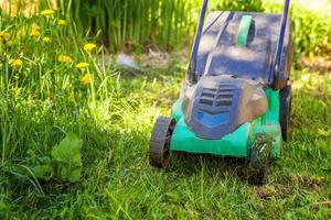 Rasenmäher, der an sonnigen Tagen grünes Gras im Hinterhof schneidet. Gartenland-Lifestyle-Hintergrund. schöne aussicht auf frischen grünen rasen im sonnenlicht, gartenlandschaft im frühling oder in der sommersaison. foto