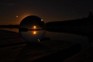 Glaskugel auf einem Holzsteg an einem schwedischen See bei Nacht. Sterne und Mond foto