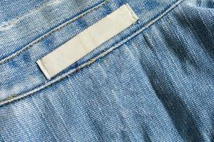 leeres weißes Wäschepflege-Kleidungsetikett auf Denim-Jeans-Texturhintergrund foto