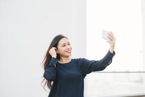 entspannt und fröhlich. Arbeit und Urlaub. Outdoor-Porträt einer glücklichen jungen Frau, die ein Smartphone benutzt, ein Selfie-Foto macht und Sie auf der Terrasse mit wunderschönem Blick auf die Stadt ansieht. foto