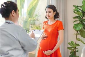 glückliche schwangere frau beratung mit arzt in der nähe des fensters
