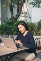 Nutzung des kostenlosen WLANs. Schöne junge Frau, die am Laptop arbeitet und lächelt, während sie im Freien sitzt foto