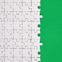 Fragment eines gefalteten weißen Puzzles auf dem Hintergrund einer grünen Kunststoffoberfläche. texturfoto mit kopierraum für text foto