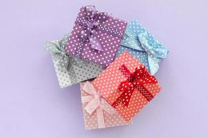 Haufen von kleinen farbigen Geschenkboxen mit Bändern liegt auf violettem Hintergrund. minimalismus flach draufsicht foto