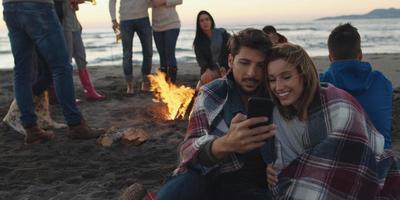 Paar genießt Lagerfeuer mit Freunden am Strand foto