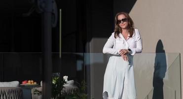 Eine Frau in Freizeitkleidung und Sonnenbrille genießt die Terrasse eines Luxushauses. selektiver Fokus foto