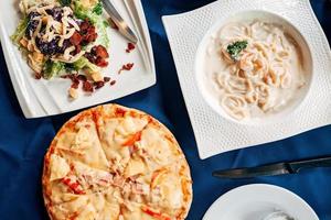 hawaiianische pizza, salat cesar und meeresfrüchte spaghetti flach gelegt. Draufsichttisch mit italienischem Essen. foto
