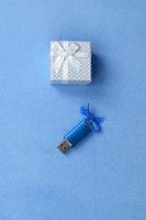 Eine brillantblaue USB-Speicherkarte mit blauer Schleife liegt neben einer kleinen Geschenkbox in Blau mit einer kleinen Schleife auf einer Decke aus weichem, flauschigem hellblauem Fleecestoff. klassisches weibliches Geschenk-Speicherkartendesign foto