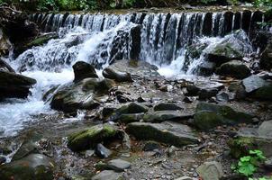 Nahaufnahme eines kleinen wilden Wasserfalls in Form von kurzen Wasserströmen zwischen Bergsteinen foto