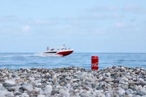 antalya, türkei - 18. mai 2021 original coca cola rote blechdose liegt auf kleinen runden kieselsteinen in der nähe der meeresküste. Coca-Cola-Dose und Schnellboot am Strand foto