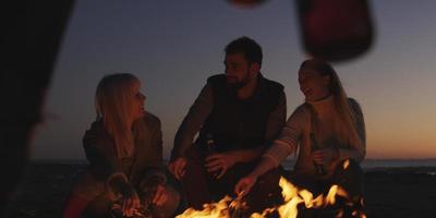 junge freunde, die am lagerfeuer am strand mit bier anstoßen foto