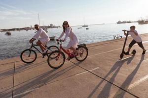 glückliche familie, die zusammen einen schönen morgen am meer genießt, eltern, die fahrrad fahren, und ihr sohn, der einen elektroroller fährt. selektiver Fokus foto