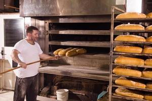 Bäckereiarbeiter, der frisch gebackenes Brot herausnimmt foto