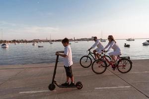 glückliche familie, die zusammen einen schönen morgen am meer genießt, eltern, die fahrrad fahren, und ihr sohn, der einen elektroroller fährt. selektiver Fokus foto