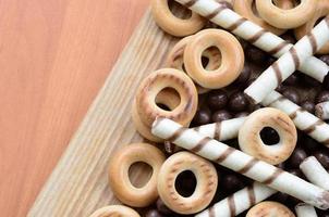 Knusprige Röhrchen, Schokoladenschmelzkugeln und Bagels liegen auf einer Holzoberfläche. Mischung aus verschiedenen Süßigkeiten foto