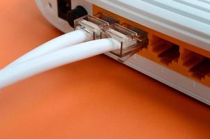 Die Internetkabelstecker sind mit dem Internetrouter verbunden, der auf einem leuchtend orangefarbenen Hintergrund liegt. Elemente, die für die Internetverbindung erforderlich sind foto