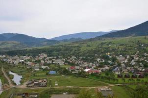 eine schöne aussicht auf das dorf mezhgorye, karpatengebiet. Viele Wohngebäude, umgeben von hohen Waldbergen und einem langen Fluss foto