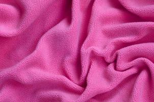 die Decke aus pelzigem rosa Fleecestoff. ein Hintergrund aus hellrosa weichem Plüsch-Fleece-Material mit vielen Relieffalten foto