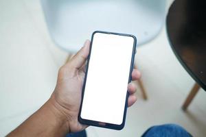 POV der Hand eines jungen Mannes mit Smartphone mit leerem Bildschirm auf einem Stuhl sitzend foto